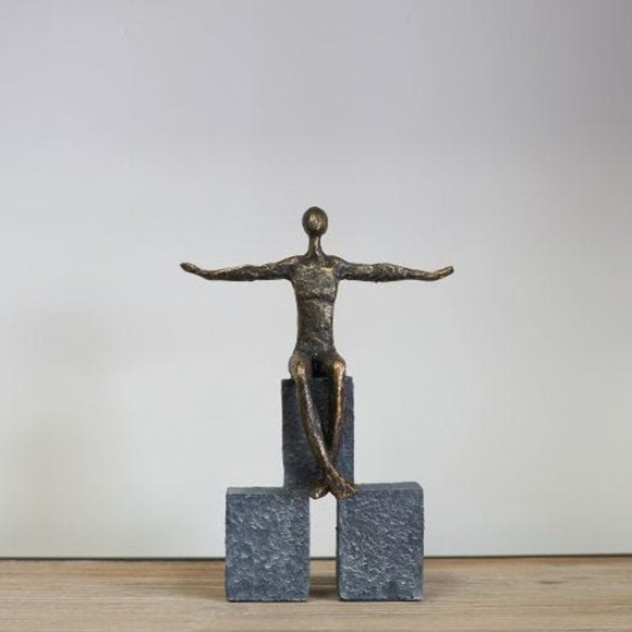 A female bronze sculpture featuring a lady with outstretched arms sitting on blocks