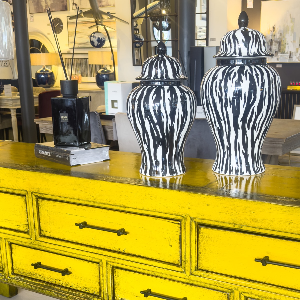 yellow painted wood sideboard with two ceramic monochrome lidded jars, fashion design book and luxury glass reed diffuser