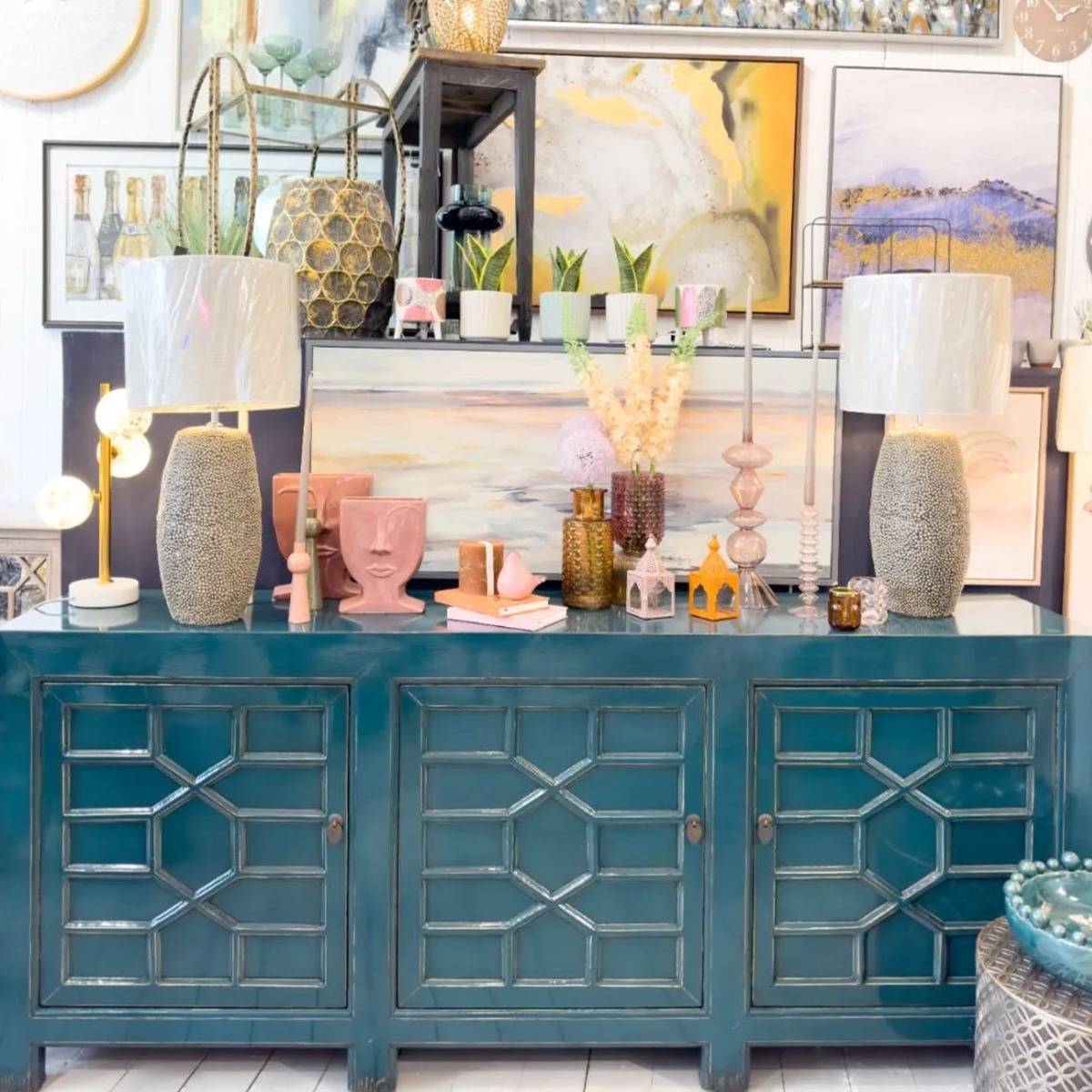 a deep blue painted wooden sideboard with pink ceramic face motif vases on top, paired with a set of neutral decorative table lamps