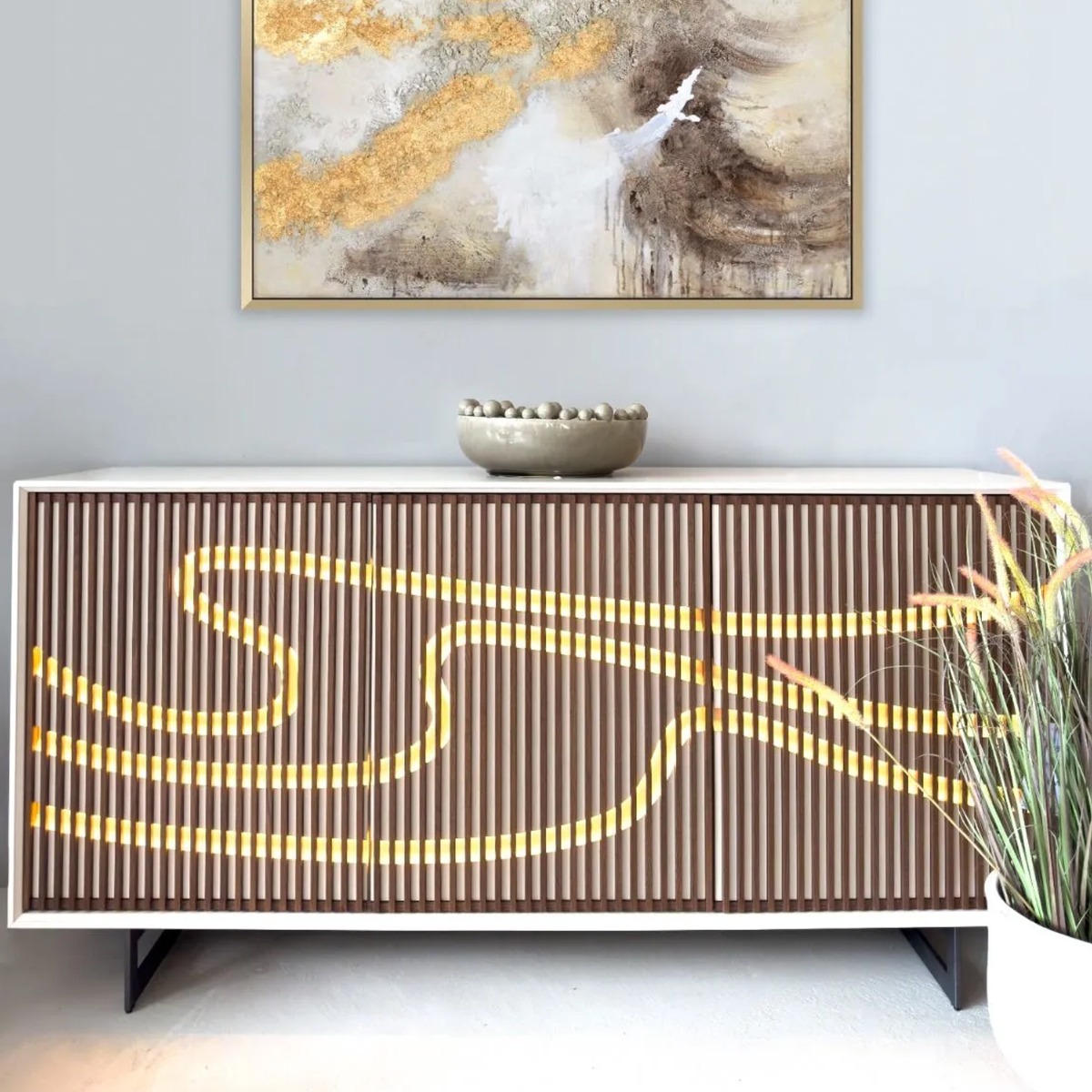 dark wood slatted sideboard with swirling LED pattern, accessorised with a glossy ceramic grey bobble bowl and an abstract gold artwork behind the sideboard