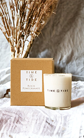 A candle sitting next to a brown paper candle box with wheat in background