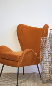 orange wing occasional chair next to silver cut vase