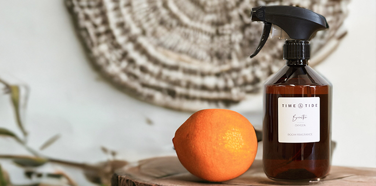 A room spray bottle sitting on a wooden plinth next to an orange