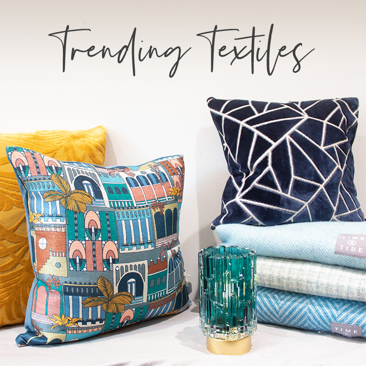 A collection of bright abstract cushions, with a pile of lambswool throws in shades of blue