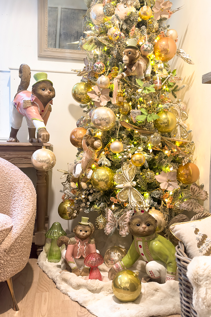 a snowy christmas tree decorated with luxurious embellished dragonfly and moth clip ons, large metallic green and pink glass baubles and pastel fairy lights. Pink and green decorative monkeys at base of tree with pink and green glass LED mushroom lights. 
