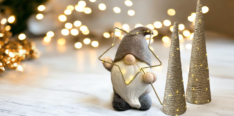 A elf with light up star statue and two gold light up cone trees on a white table with golden sparkles in the background