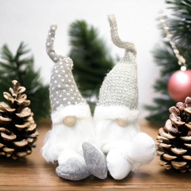 Two white elf christmas decorations next to a pinecone sitting on a wooden table