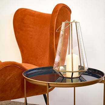 blue enamel top side table with gold legs, next to orange chair with gold lantern on top