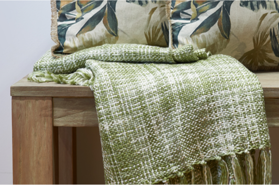 folded green woven throw on bench with leaf print cushions